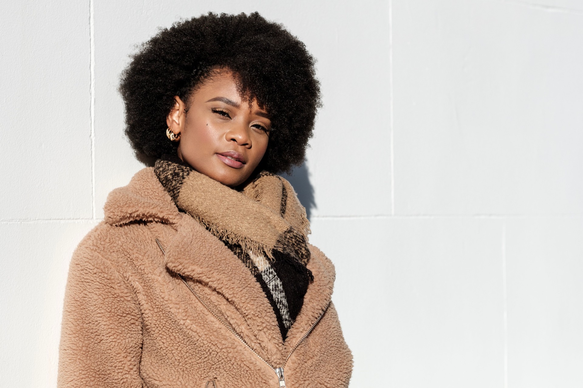 Confident young model looking at camera leaning on a white wall outdoors.