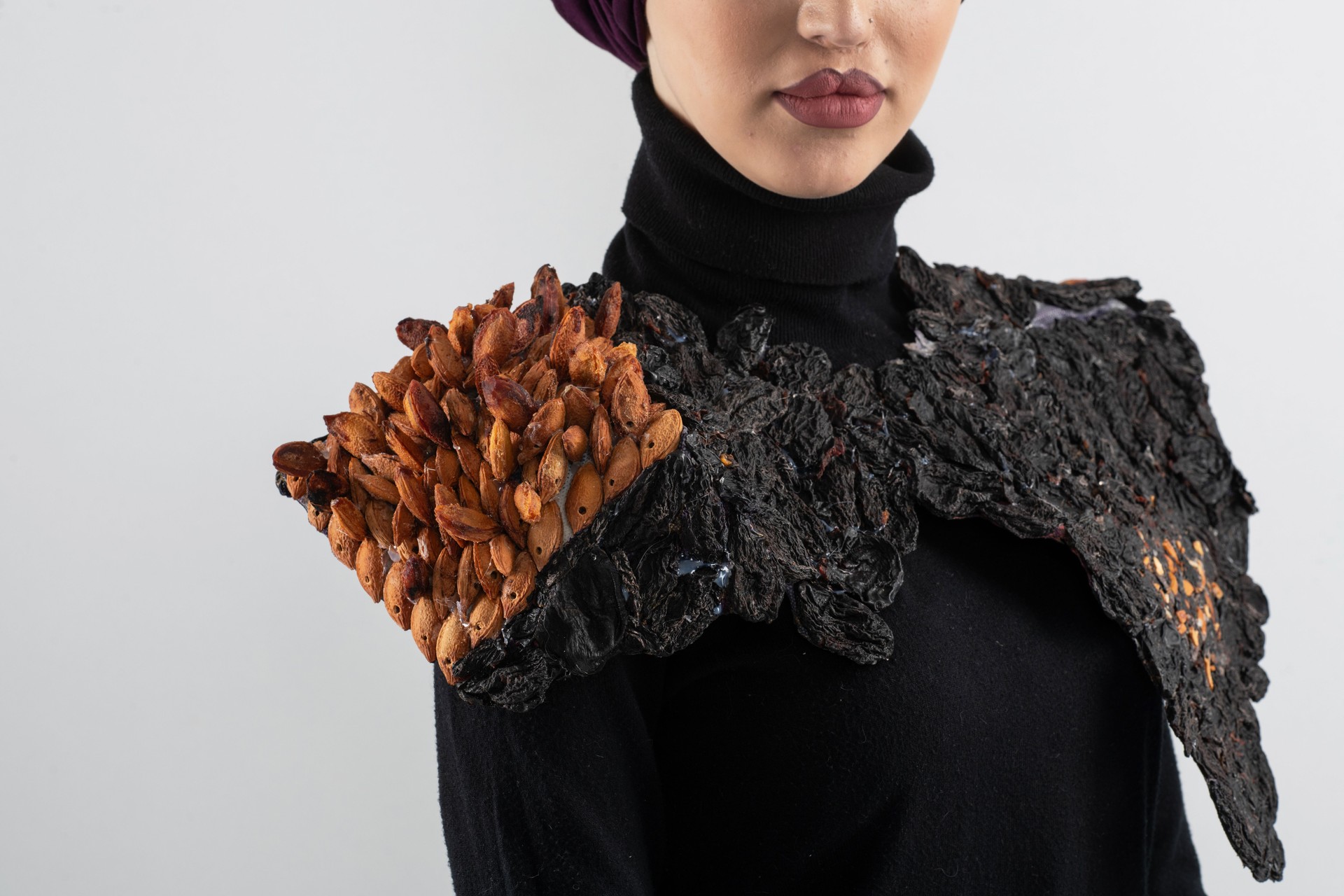 A stylish Muslim woman in a hijab presents her innovative handmade fashion accessory crafted from dried plums in a professional studio.