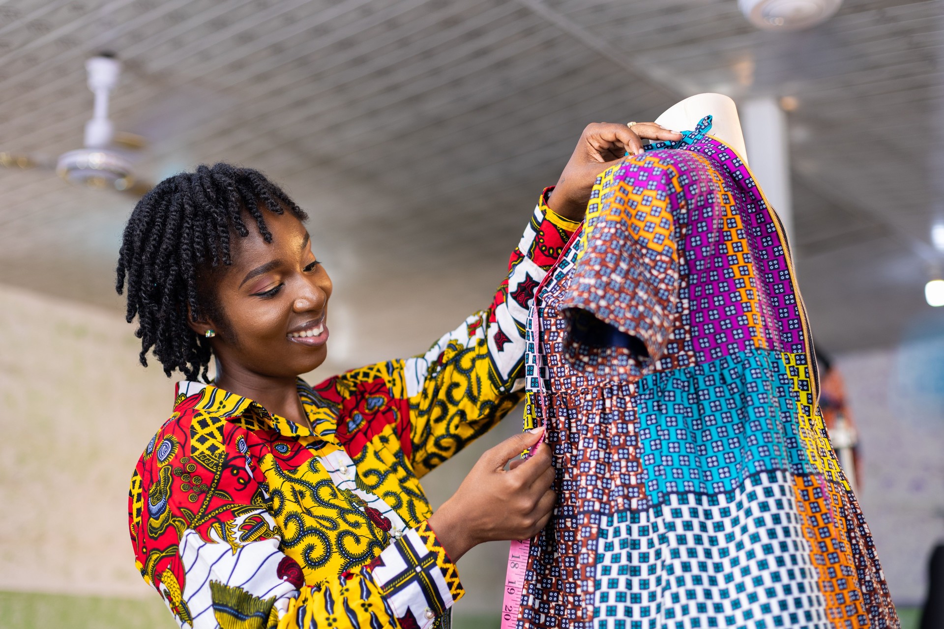 Smiling Ghanaian Dressmaker with African pattern dress in her studio